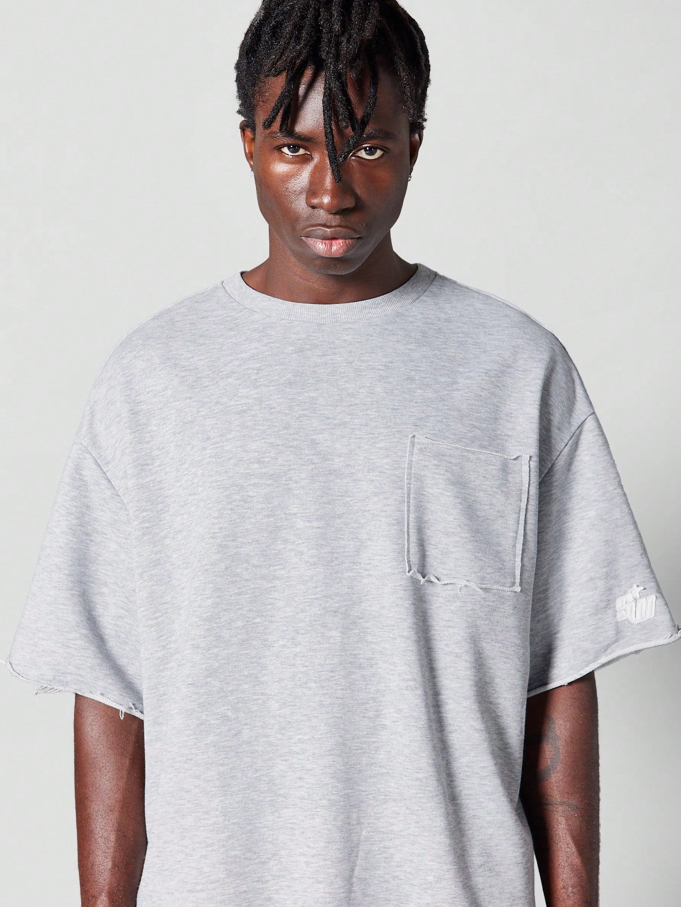 Oversized Fit Raw Edge Tee With Front Pocket And Sleeve Applique